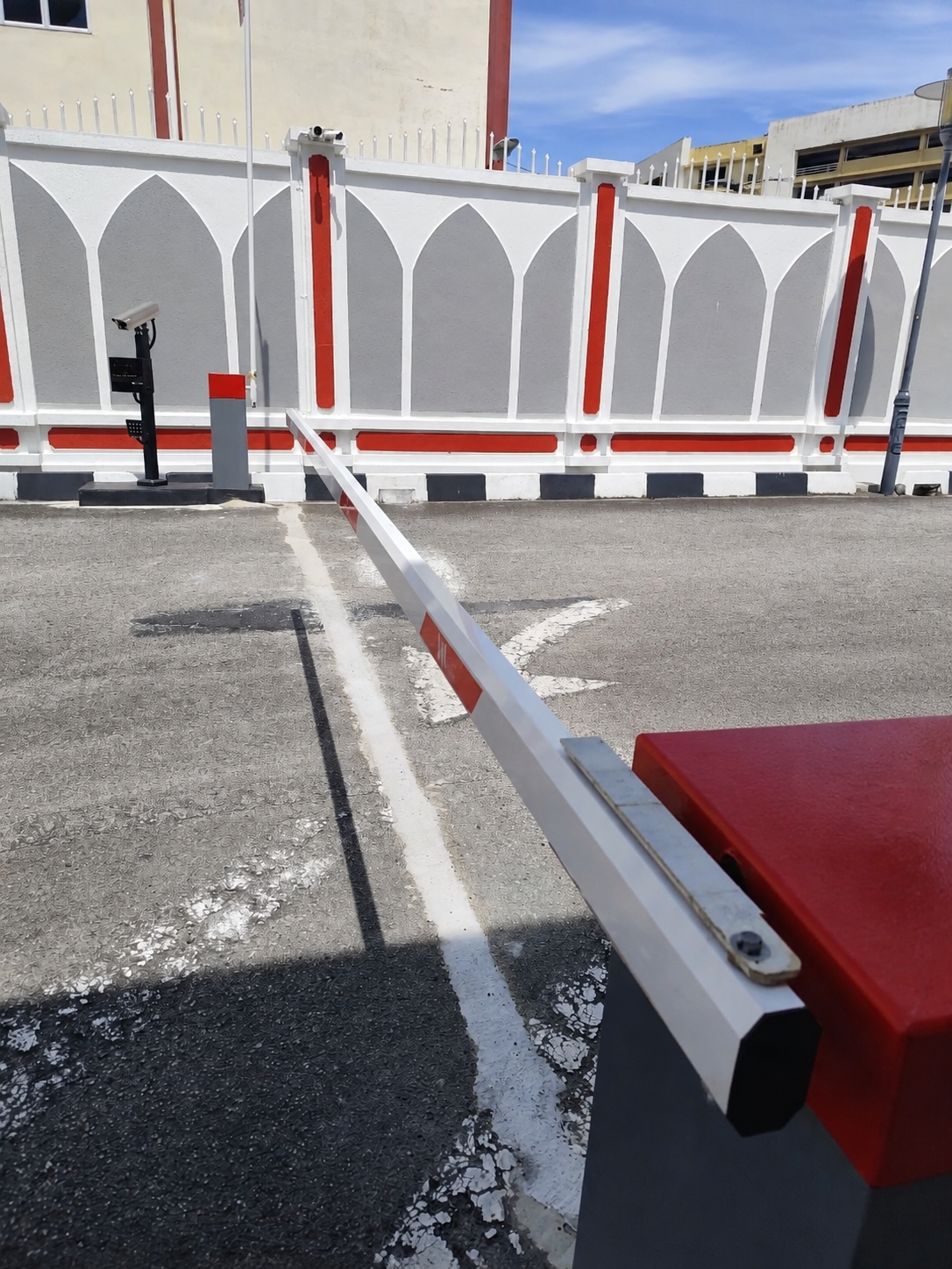 Barrier arm lowered across the entrance lane, with camera poles mounted along the perimeter wall